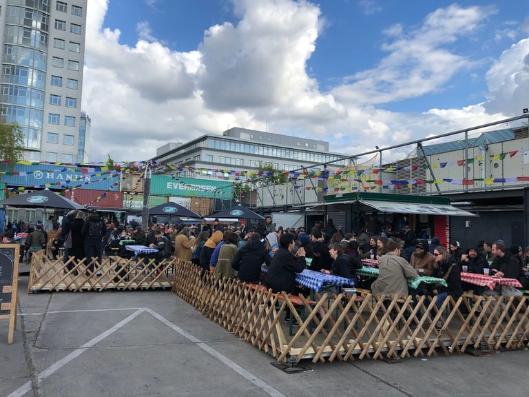 Open-Air-Markt mit Holzbarrieren, Verkaufsständen und Menschenmassen beim Einkaufen an einem sonnigen Tag